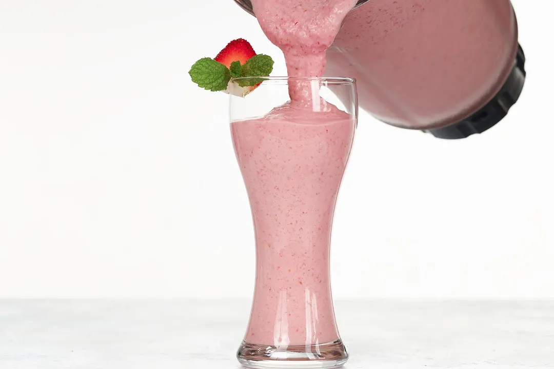 pouring pink smoothie from pitcher into glass