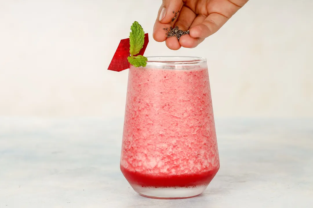 a hand holding chia seeds and a glass of beet smoothie