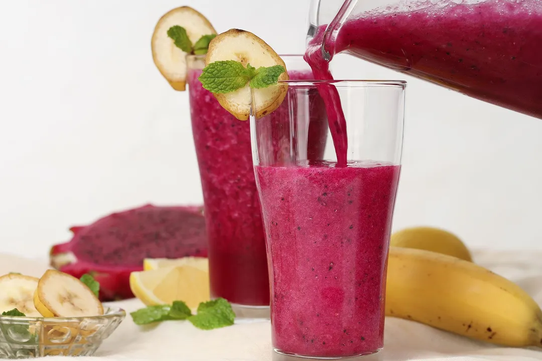 a pitcher pouring red smoothie into a glass