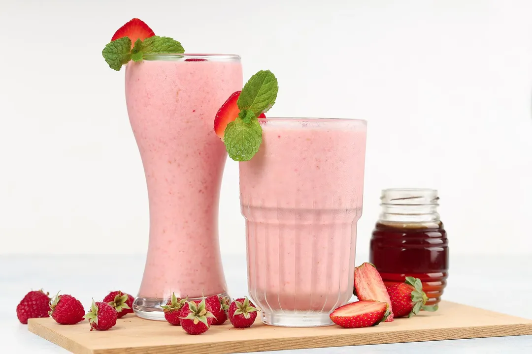 two glass of strawberry raspberry smoothie and a jar of honey on a tray