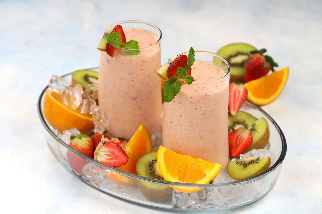 Kiwi Quencher Tropical Smoothie on a glass tray garnished with half kiwi, strawberry and sliced orange