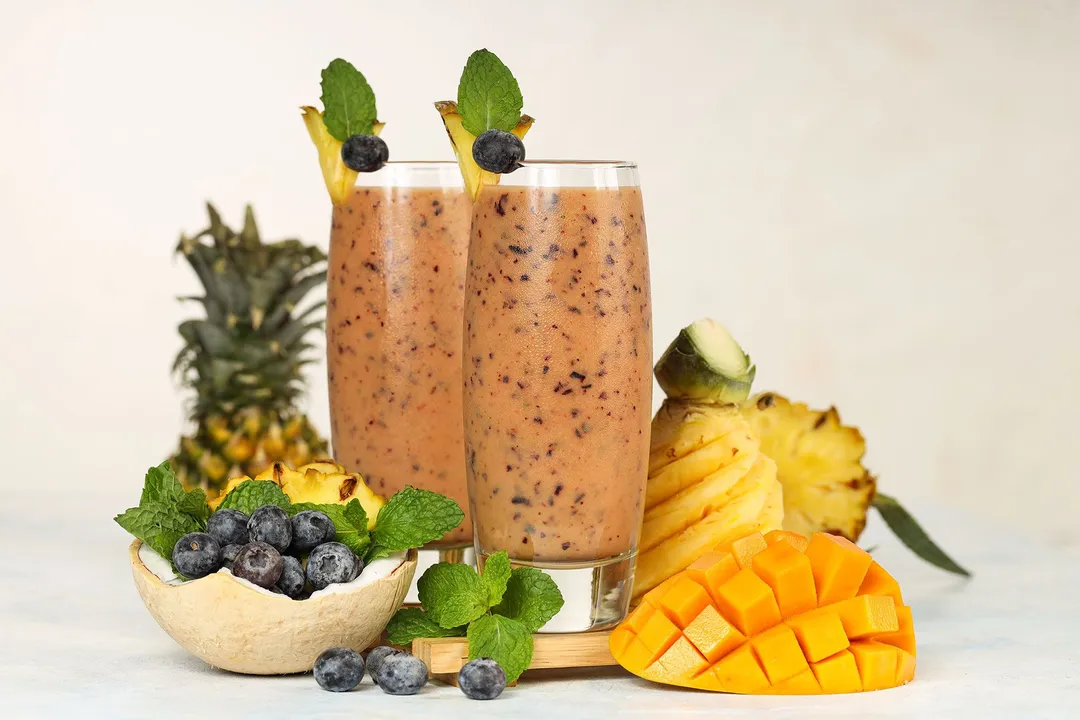 two glasses of blueberry mango smoothie decorated with mango cubed, pineapple, blueberries