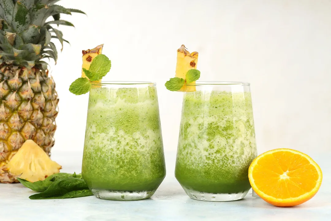two glasses of pineapple spinach smoothie decorated with half orange, pineapple