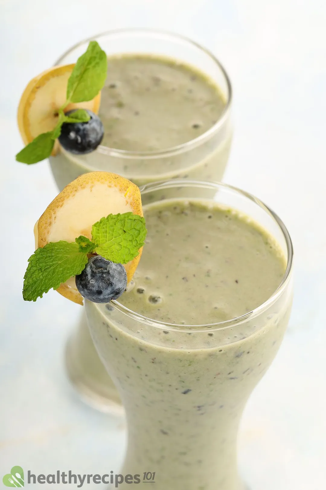 two glasses of blueberry kale smoothie decorated with blueberry, banana and mint leaves