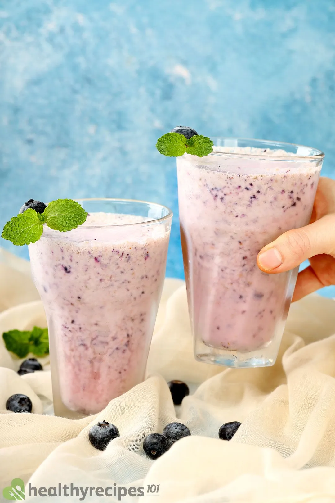 two glasses of blueberry yogurt smoothie, hand hold one