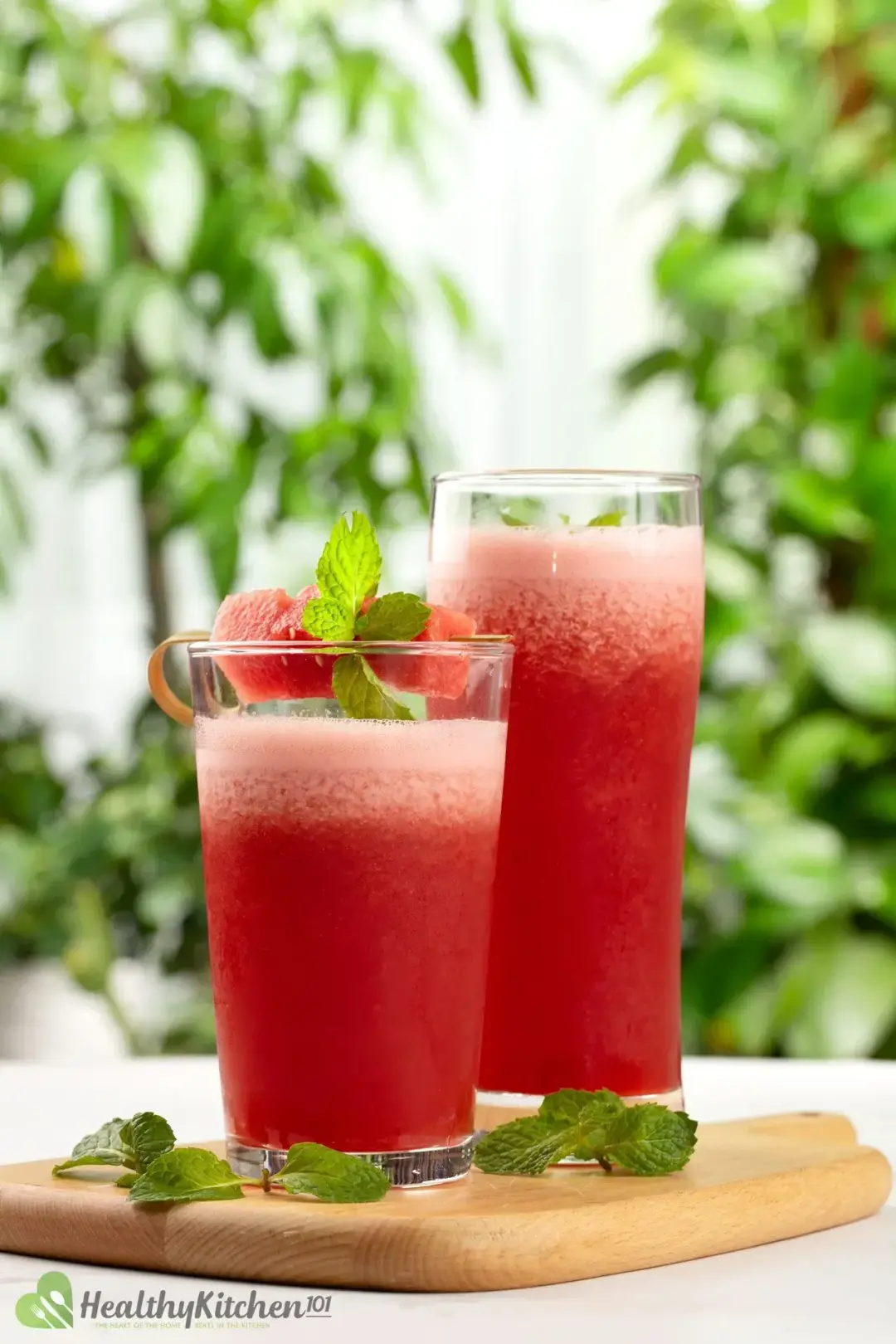 Two glasses of watermelon smoothie adorned with watermelon cubes on top of a wooden board
