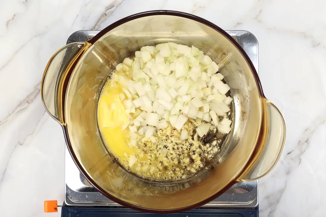 diced onion, garlic and butter cooking in a glass pot