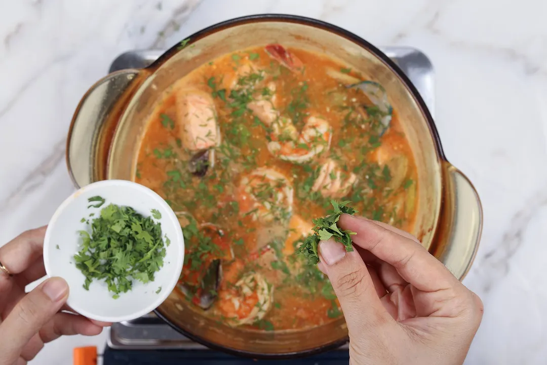 sprinkle parsley from a small bowl onto a pot of soup