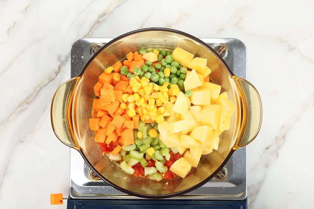 cooking potatoes cubes, carrots corn, celery and peas in a pot