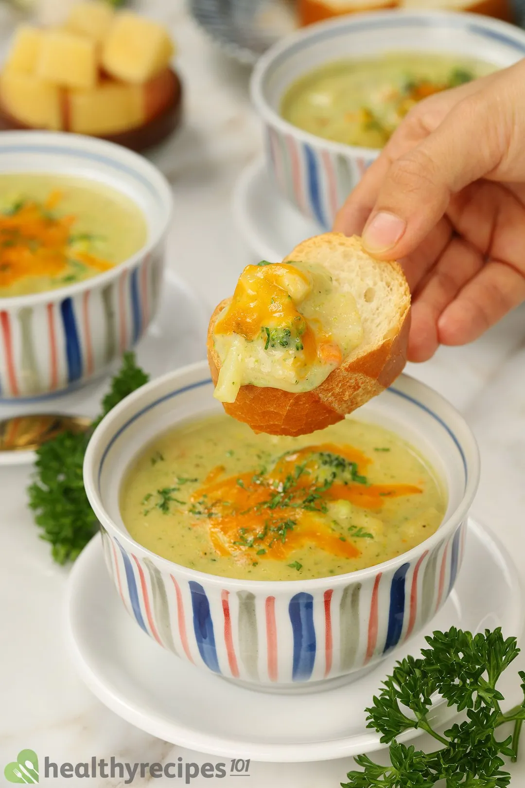 One hand holds a slice of bread on a bowl of soup